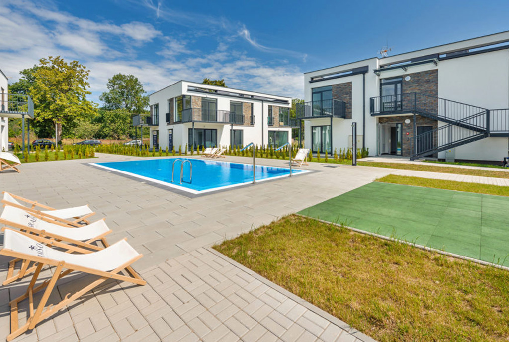 widok od strony basenu na budynek, w którym znajduje się oferowany do sprzedaży ekskluzywny apartament nad morzem