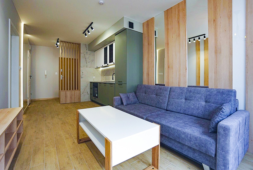 Na pierwszym planie salon w oddali aneks kuchenny w ekskluzywnym apartamencie do wynajęcia Konin.